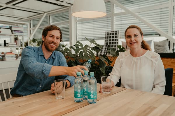 Zwei Personen sitzen an einem Tisch und in der Mitte sind Wasserflaschen von share aufgestellt.