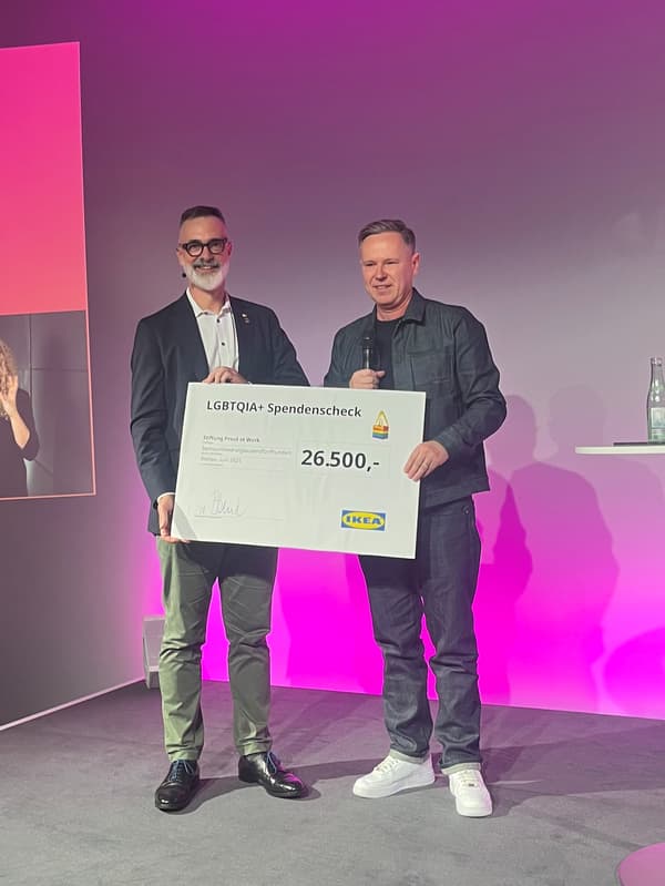 Zwei Personen stehen auf einer Bühne und halten einen symbolischen Spendenscheck über 26.500 € hoch.