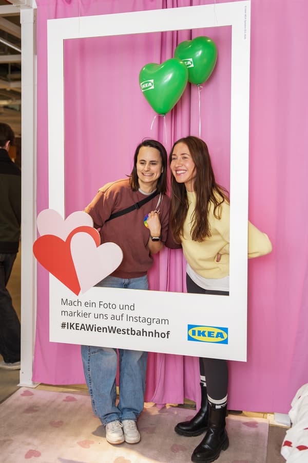 Zwei Personen stehen bei einem Fotospot hinter einem Kartonrahmen mit der Schrift: Mach ein Foto und markier uns auf Instagram #IKEAWienWestbahnhof