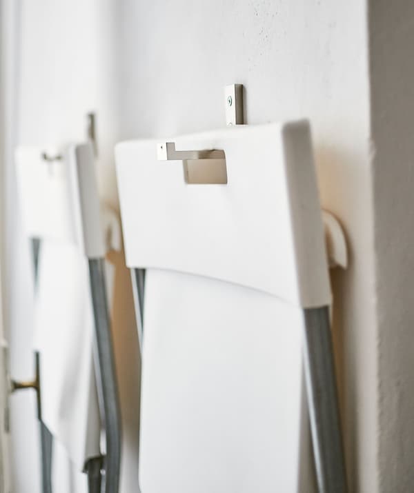 Zwei unserer GUNDE Klappstühle in Weiss, die an BJÄRNUM Haken an einer Wand hängen.