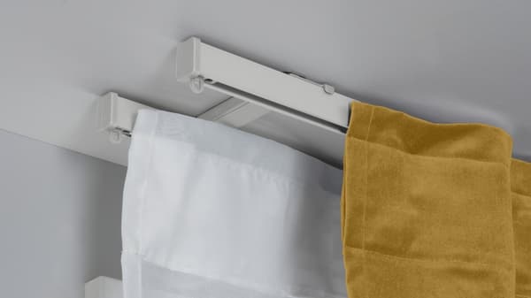 Zwei weiße VIDGA 1-läufige Gardinenschiene sind mit einer VIDGA Deckenbefestigung für 2 Gardienenschienen an einer weißen Zimmerdecke montiert. Daran hängt ein transparenter und ein blickdichter Vorhang. 