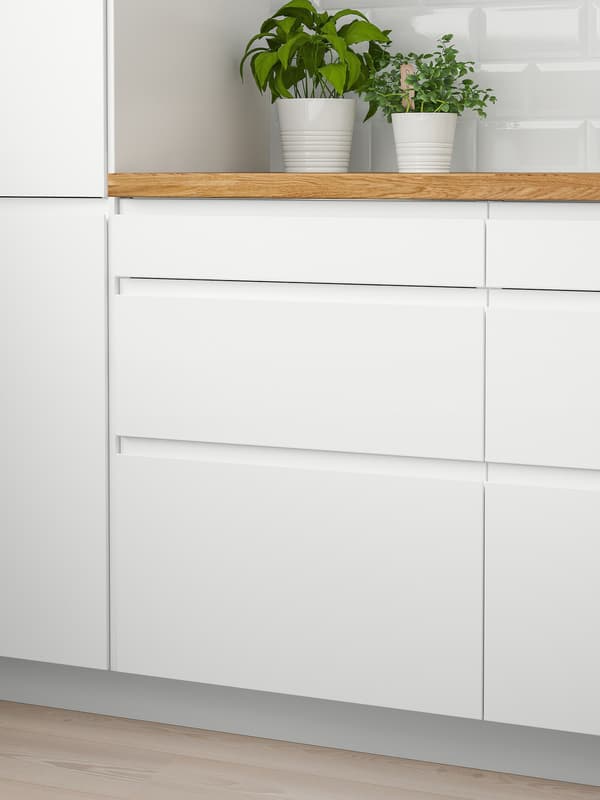 Zwei weiße Wandschränke mit den VOXTORP Türen in Mattweiß, eine Arbeitsplatte aus Holz und zwei Töpfe mit Kräutern darauf.