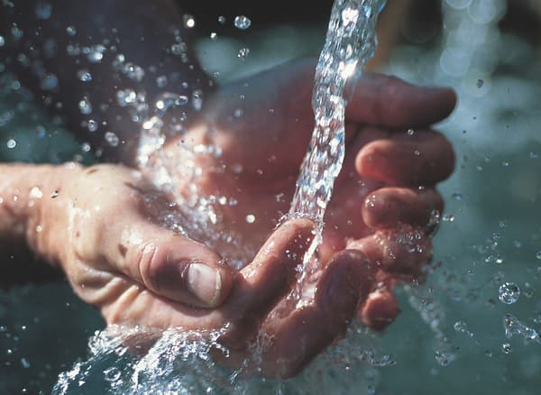 زوج من الأيد في محاولة للإمساك بالمياه من حنفية مفتوحة.