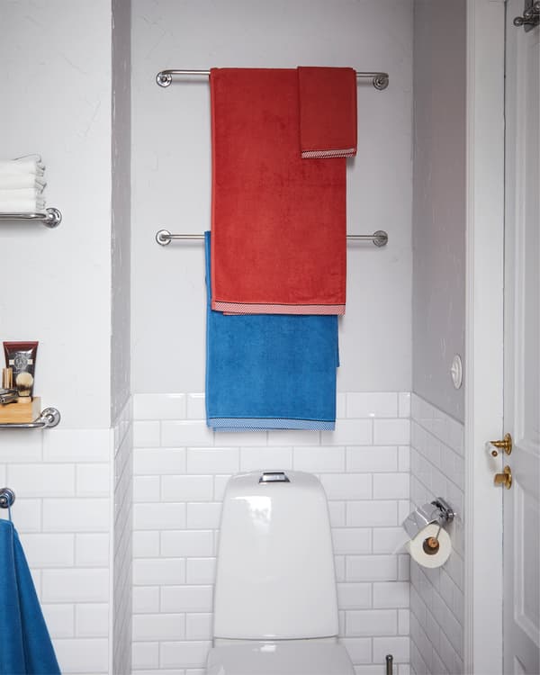 زوج من سكك المناشف VOXNAN بتأثير الكروم موضوعة على الحائط فوق مقعد الحمام مع تعليق مناشف حمام عليها.