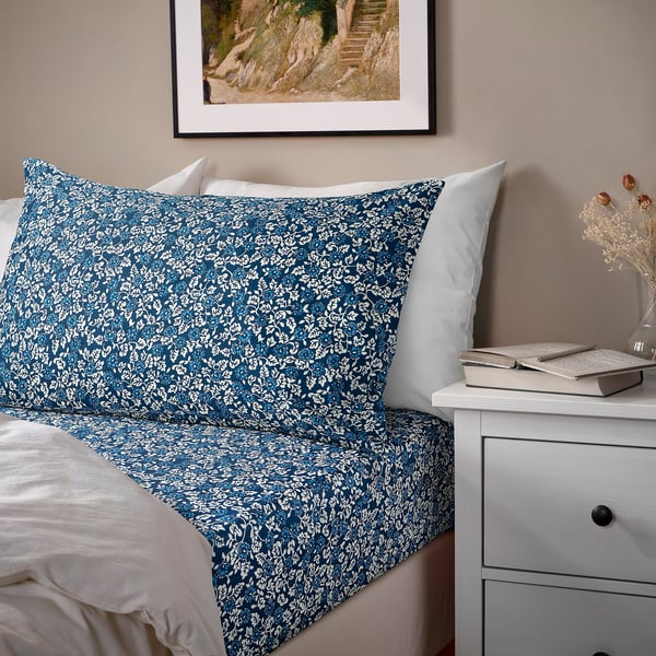 ÄLSKEBLÅMME blue floral bedding set on bed, framed wall art, bedside drawer with items.