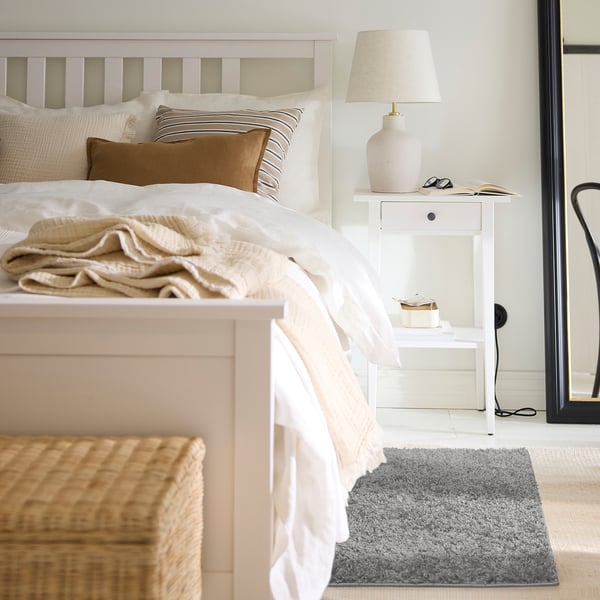 Bedroom with white bed, grey ÄRENDE rug, beige pillows, and wooden floor.