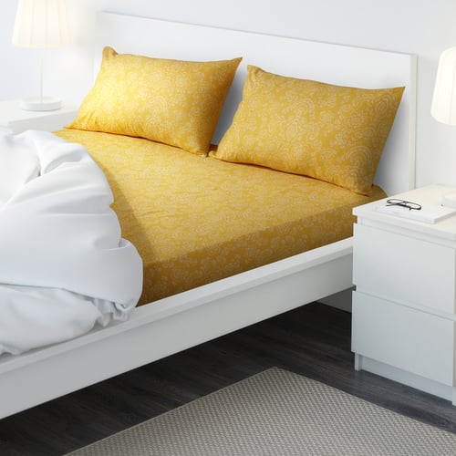 Neat bed with yellow floral sheets, two pillows, bedside table with lamp.