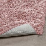 Pink plush bath mat with white textured non-slip backing.