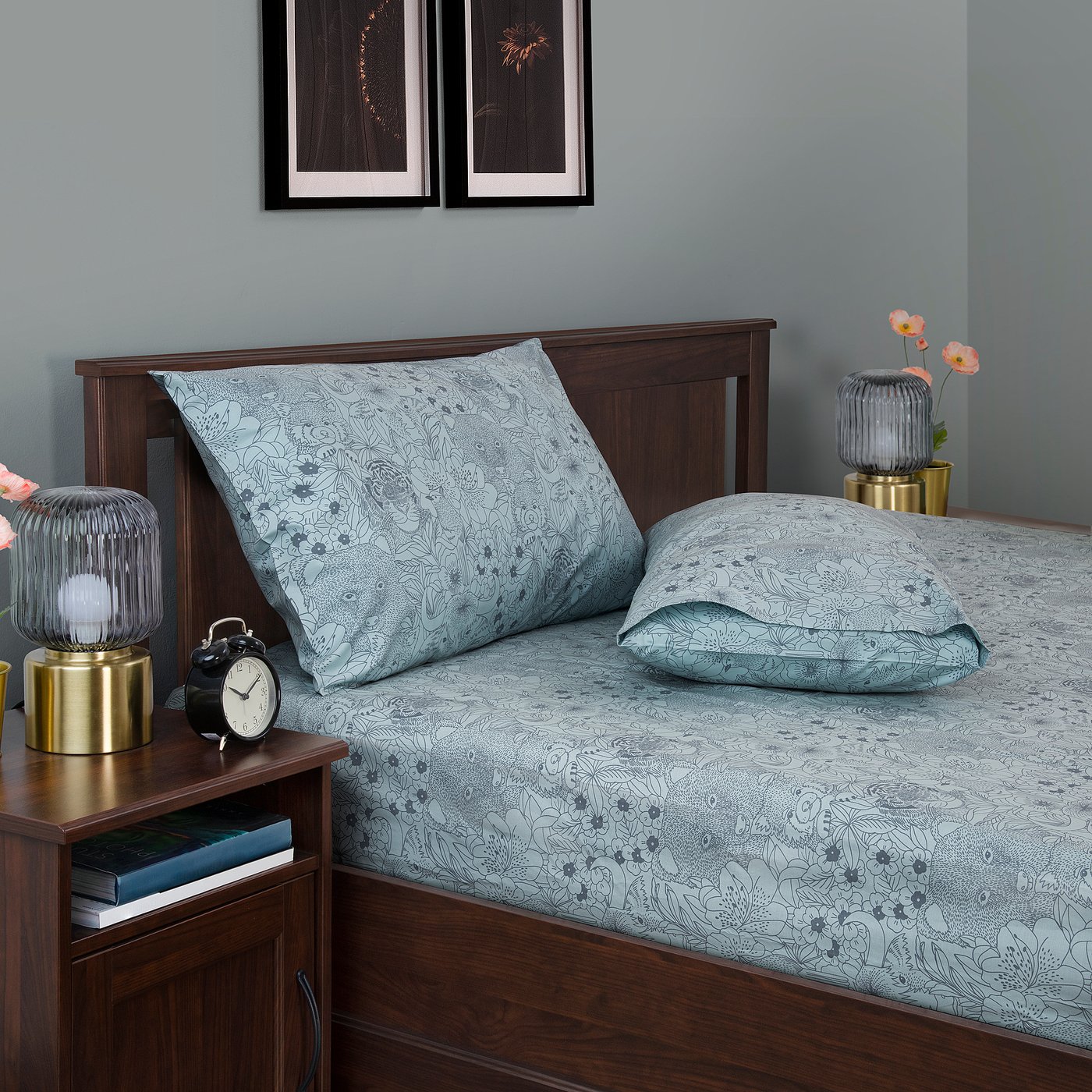 Cosy blue floral bedding set with wooden headboard, small bedside table with clock and lamp.