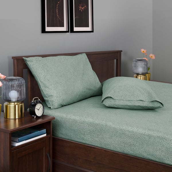 Green-dotted bed with wooden headboard, bedside lamps, and clock.