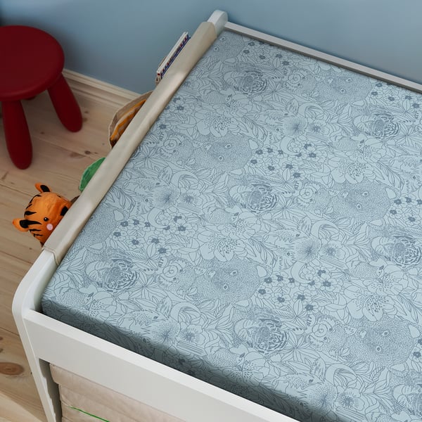 A white toddler bed with blue floral-patterned bedding, showing a toy tiger and a small red stool.