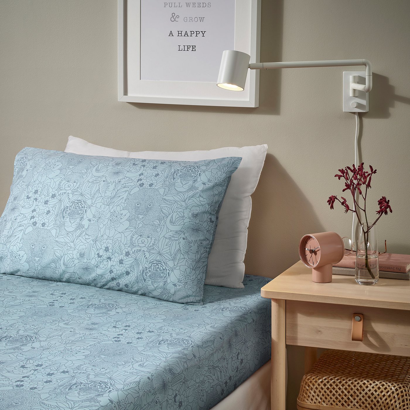 Cosy bed with blue floral print, pink clock, flowers, and wall light. Or, even shorter: blue floral bed with pink clock and flowers.