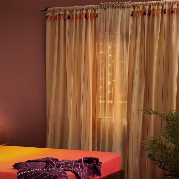 Vibrant AROMATISK curtain, beige with tassels, fully covers tall window, highlights room decor.