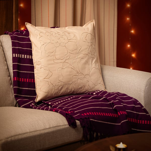 Cosy living room corner with beige throw pillow, floral design, on grey chair. Purple blanket and string lights.
