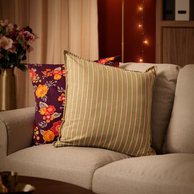 Beige sofa with green & pink striped AROMATISK cotton cushion, purple floral cushion nearby, and vase with flowers.
