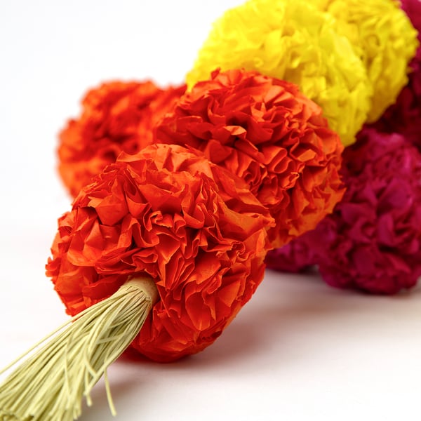 Bright, handmade paper flowers in orange, yellow, and pink, arranged closely together, showcasing intricate details and vibrant colours.