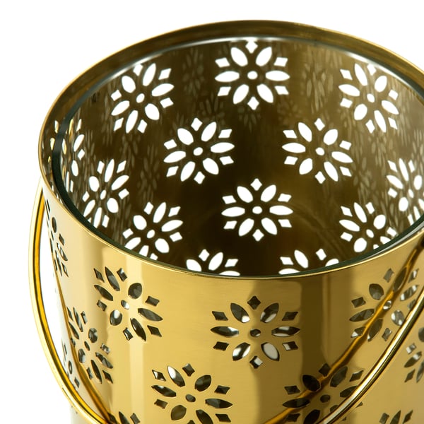 Golden metal lantern with intricate floral cutouts, reflecting light and shadow, sitting elegantly.