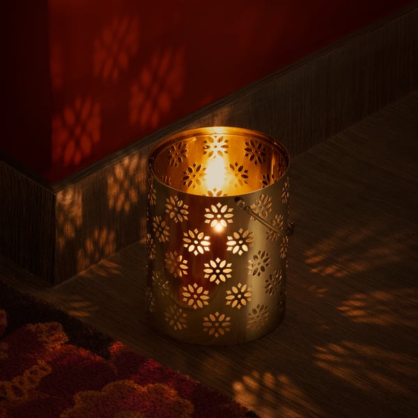 A golden lantern with floral cutouts casts warm, glowing light and intricate shadows on the wooden floor and red wall, creating a cosy ambiance.