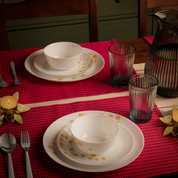 Table set with white dishes, pink glasses, and red placemats; candles and cutlery included.