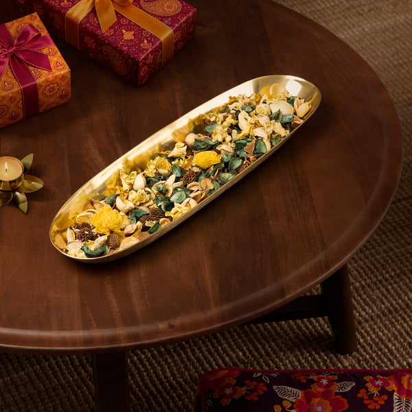 Oval decorative dish on a table, filled with flowers, near gifts and a lit candle.