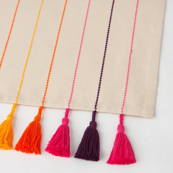 Colourful tassels hang from a beige table runner with vibrant stripes. The fabric appears soft and well-crafted.