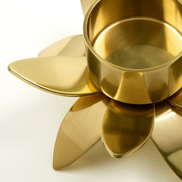Gold metal tealight holder with four curved petal-like designs, elegant and polished, reflecting light.