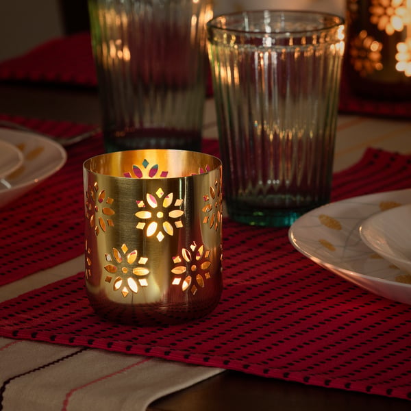 A lit gold tealight holder with floral cutouts casts warm shadows on a festive table setting.