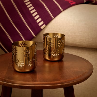 Two gold floral tealight holders on wooden table, warm glow.