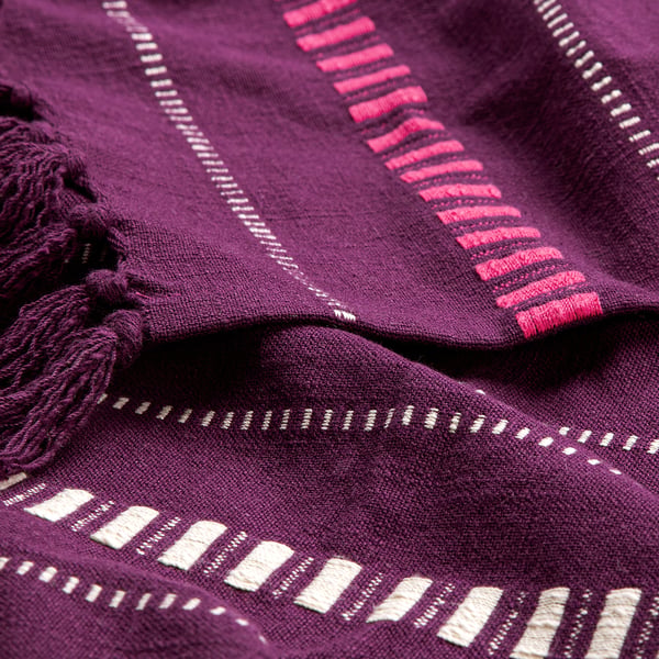 Purple cotton throw with intricate white patterns, tassels, and pink stripes, draped to show texture.