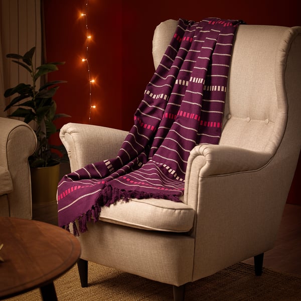 Beige armchair with patterned purple throw blanket, perfect for cozying up on chilly days.