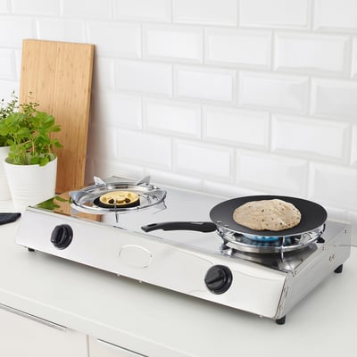 Gas cooker with two burners on counter, one griddle and one frying pan, against white-tiled wall.