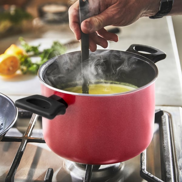 In a person stirs a pot on the stove. The red pot with steam shows the non-stick coating and even heat distribution in use.
