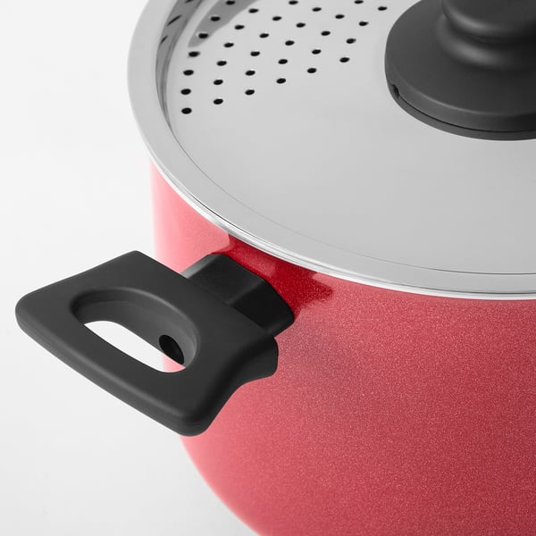 Close-up of red pot with black handle and silver lid featuring steam holes.