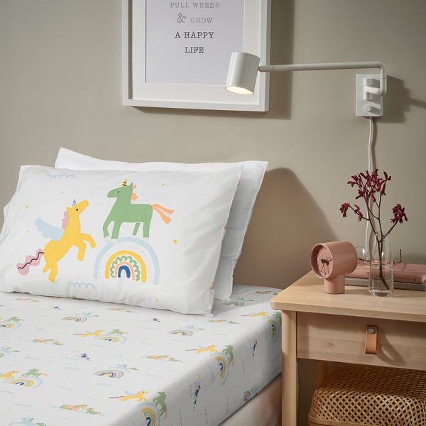 White BARNDRÖM pillowcase with unicorns & rainbows on bed.
