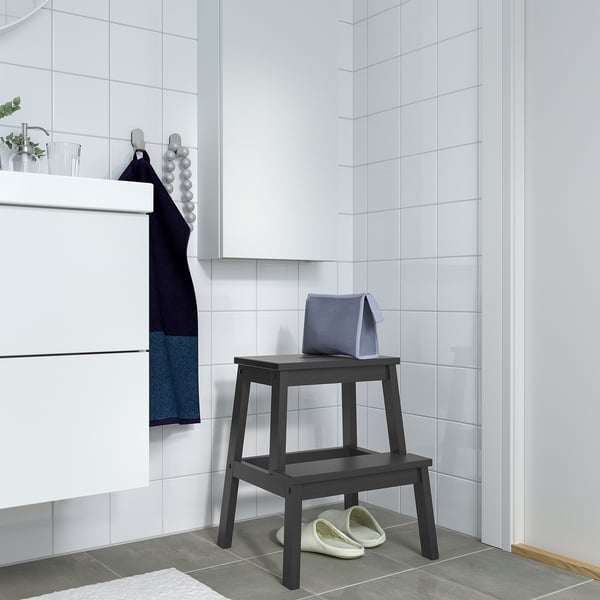 Modern bathroom with BEKVÄM black wood step stool, blue towel, white slippers. Tiled walls and floor.