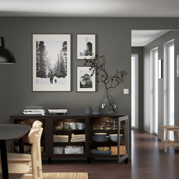 Modern dining room with dark grey walls, featuring a stylish dark wood sideboard displaying plates, mugs, and a large decorative vase with branches.