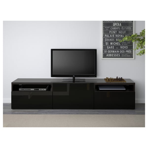 Black tv stand with drawers and cable management, holding a flat-screen tv and chess set.