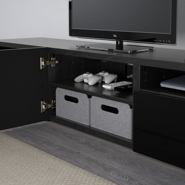 Black tv stand with drawers and storage, holding gaming controllers and cables.