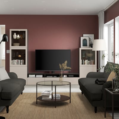 Modern living room: large tv on maroon wall, black sofas, round glass table, leafy plant, books, soft lighting.