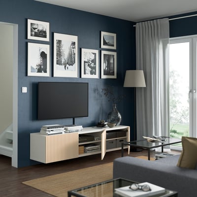 Modern living room with dark blue walls, a large tv on a white stand with birch doors, black coffee table, and framed photos.