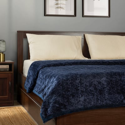 Bed with BLIXABACKEN navy blanket, two cream pillows, wooden headboard, bedside table with lamp.