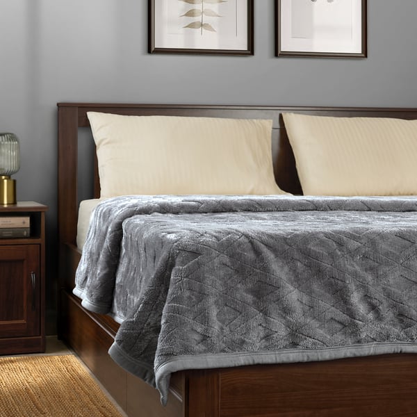 Bed with grey blanket, cream pillows, wooden headboard & gold lamp.
