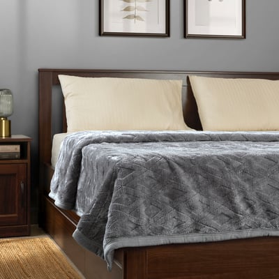 Bed with grey blanket, cream pillows, wooden headboard & gold lamp.