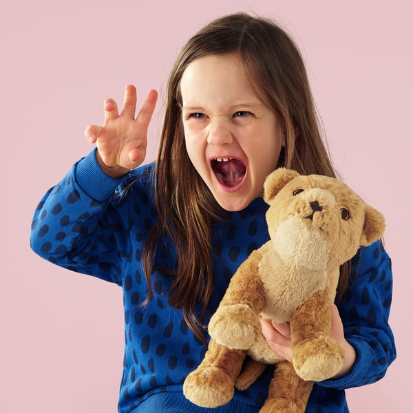 Young girl in blue dress holds soft toy lion, smiling broadly.