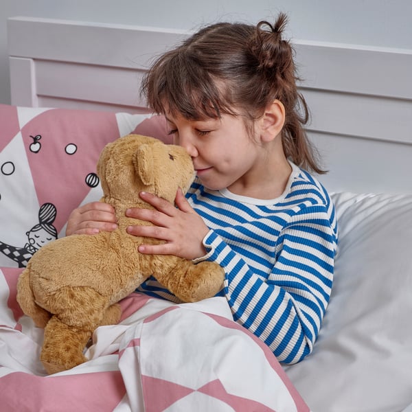 A young girl hugs a soft teddy bear while lying in bed, showcasing the comforting and cuddly nature of the toy.