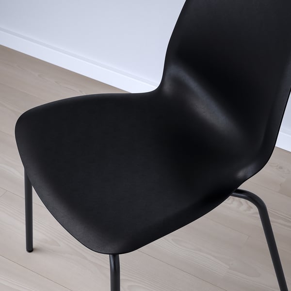 Black modern chair with sleek, curved design sits on light wooden floor.