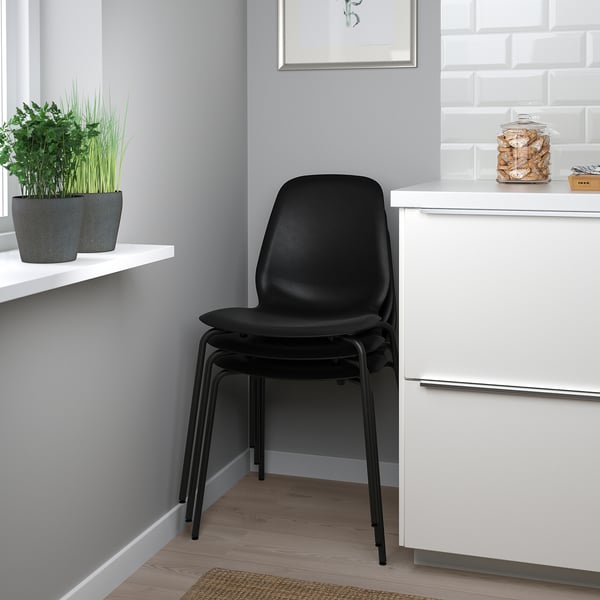 Stacked black chairs next to white cabinet with plants on shelf.