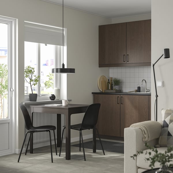 Modern dining set with extendable table and black chairs. Tables wooden top matches dark brown cabinetry; space-saving, sleek design.