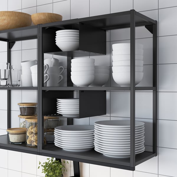 Black metal wall-mounted kitchen storage unit with three shelves holding neatly stacked white dishes, bowls, mugs, and jars.