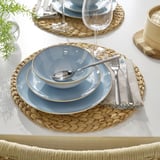 Table setting with blue plates, bowls, and glasses on woven placemats.
